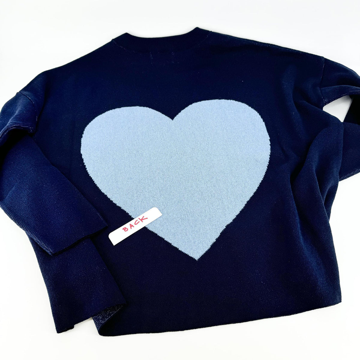 A navy pullover sweater with 'KC' written on the front and a heart shape on the back, displayed on a hanger.