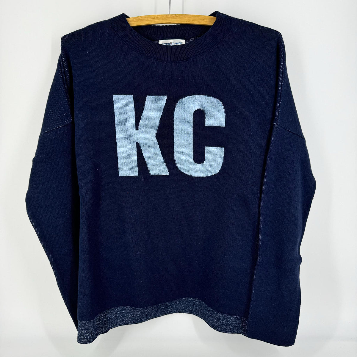 A navy pullover sweater with 'KC' written on the front and a heart shape on the back, displayed on a hanger.