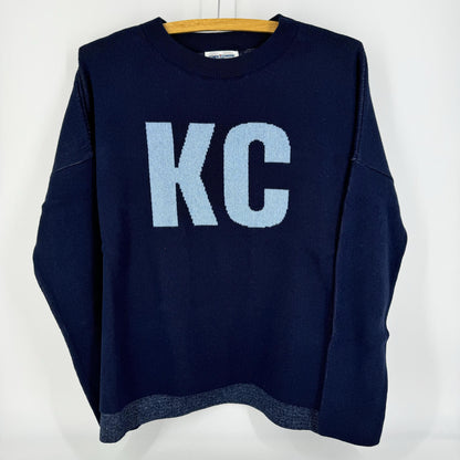 A navy pullover sweater with 'KC' written on the front and a heart shape on the back, displayed on a hanger.