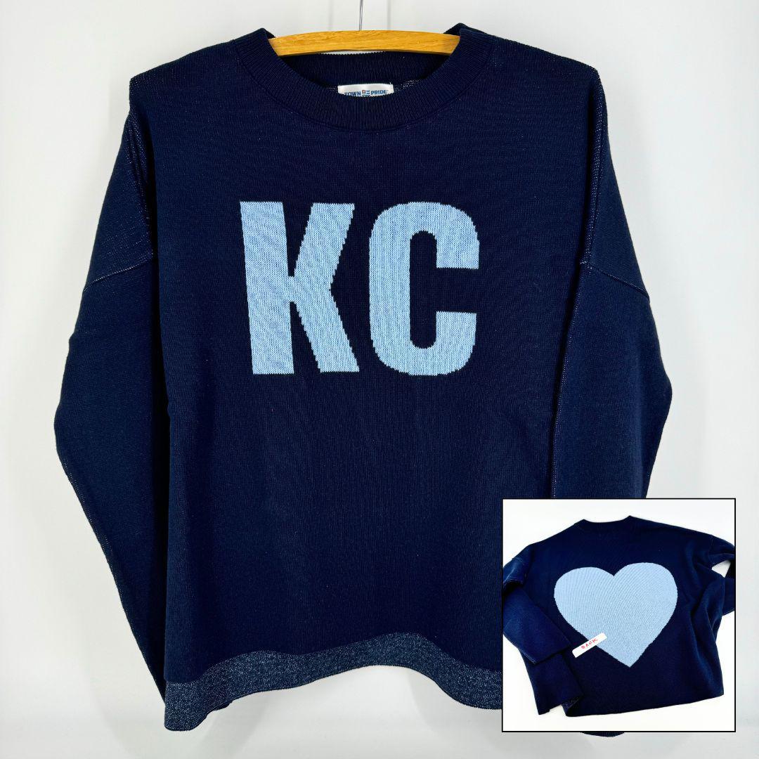 A navy pullover sweater with 'KC' written on the front and a heart shape on the back, displayed on a hanger.