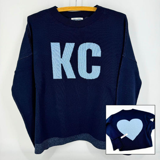 A navy pullover sweater with 'KC' written on the front and a heart shape on the back, displayed on a hanger.