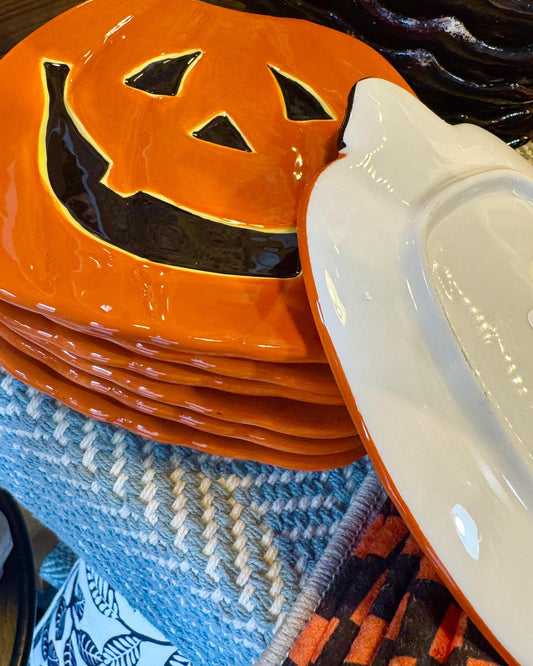 A stack of glossy orange ceramic plates with a jack-o'-lantern face cutout.