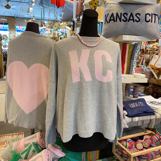 Two gray sweaters on mannequins with 'KC' and heart designs in a store setting.