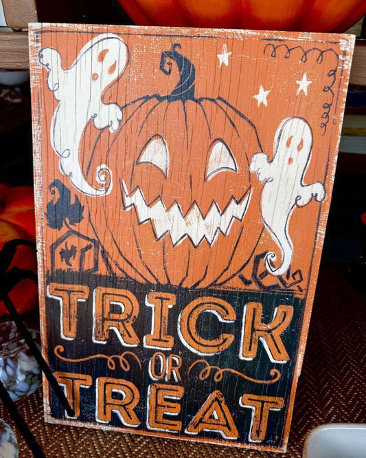 A rectangular Halloween sign with a distressed orange and black wood look, featuring a carved pumpkin, white ghosts, stars, and the words “TRICK OR TREAT” in large orange letters.
