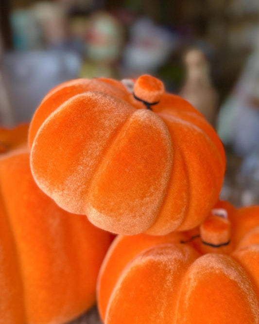 Close-up of small orange velvet pumpkins stacked together, with a soft blurred background.