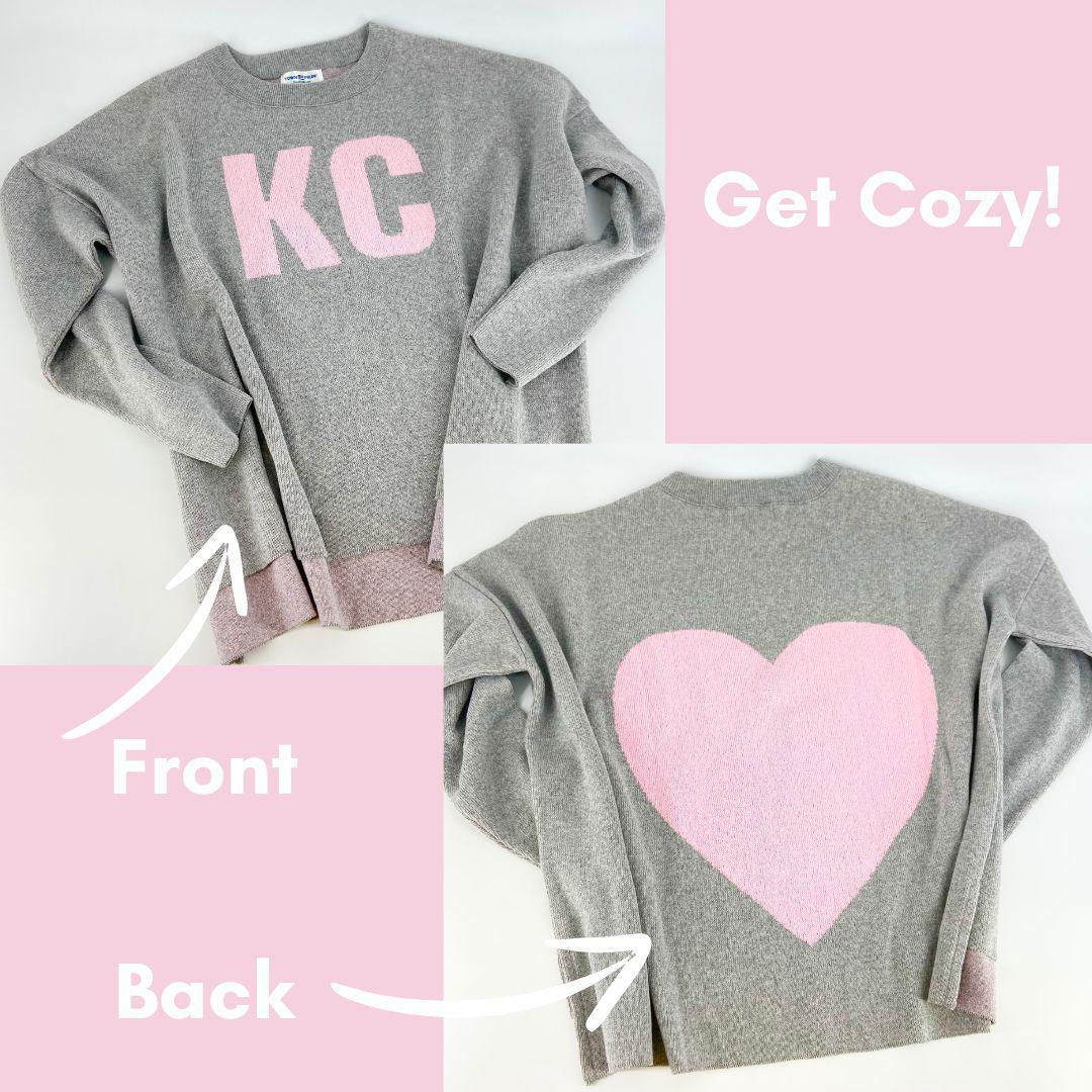 Gray sweatshirt with 'KC' on the front and a pink heart on the back, labeled 'Get Cozy!'.