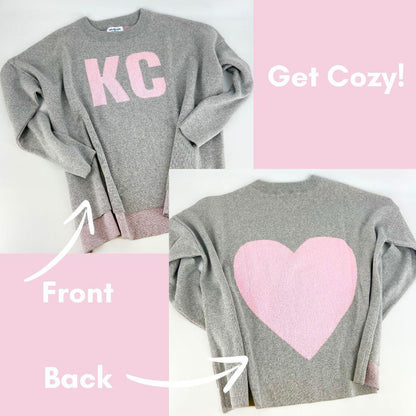 Gray sweatshirt with 'KC' on the front and a pink heart on the back, labeled 'Get Cozy!'.