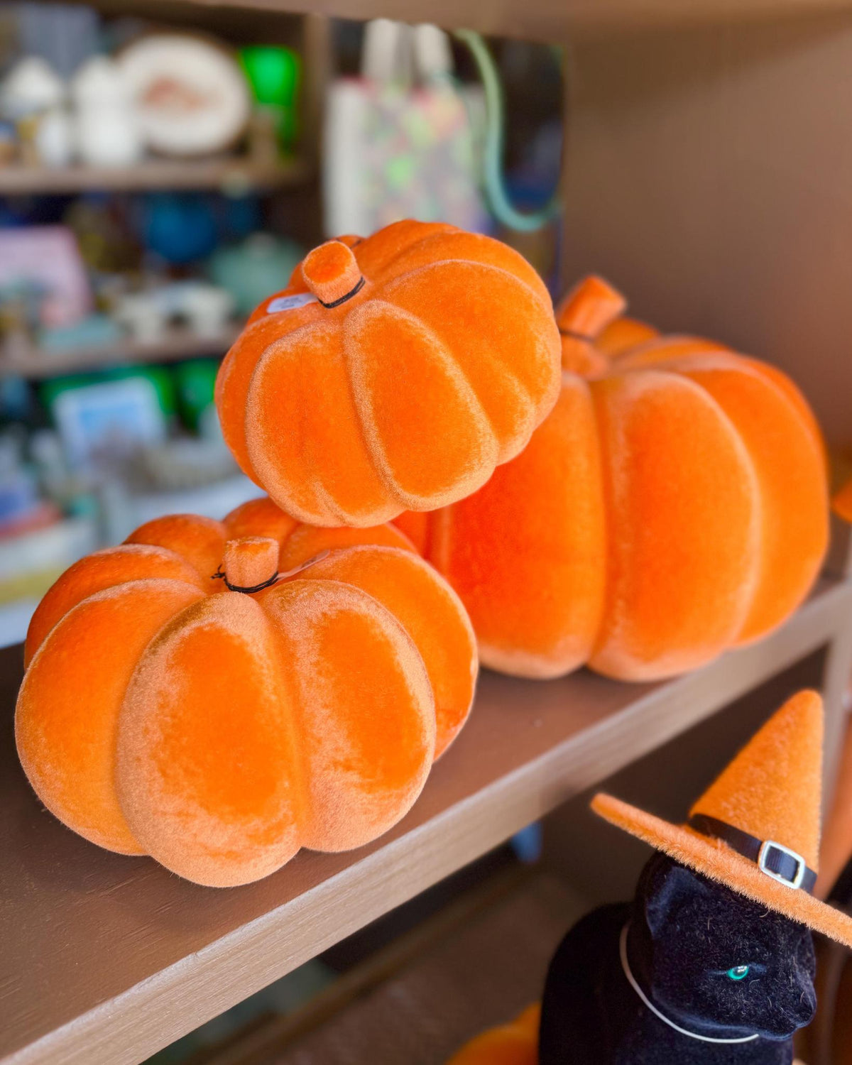 Three plush orange pumpkins displayed on a wooden shelf. Felted decoration for Fall.