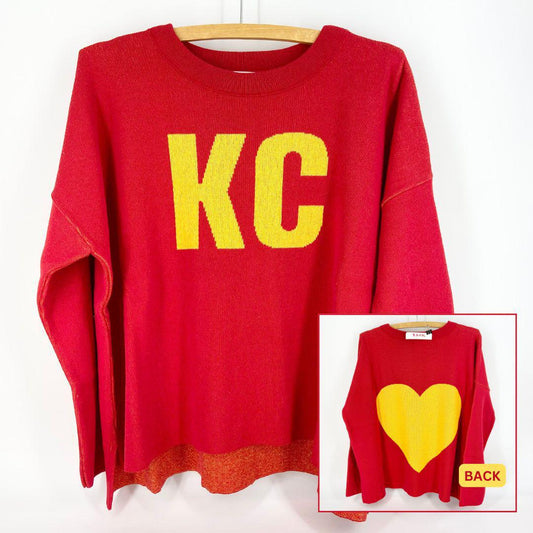 A red and gold pullover sweater with 'KC' text on the front and a heart shape on the back, displayed on a wooden hanger.