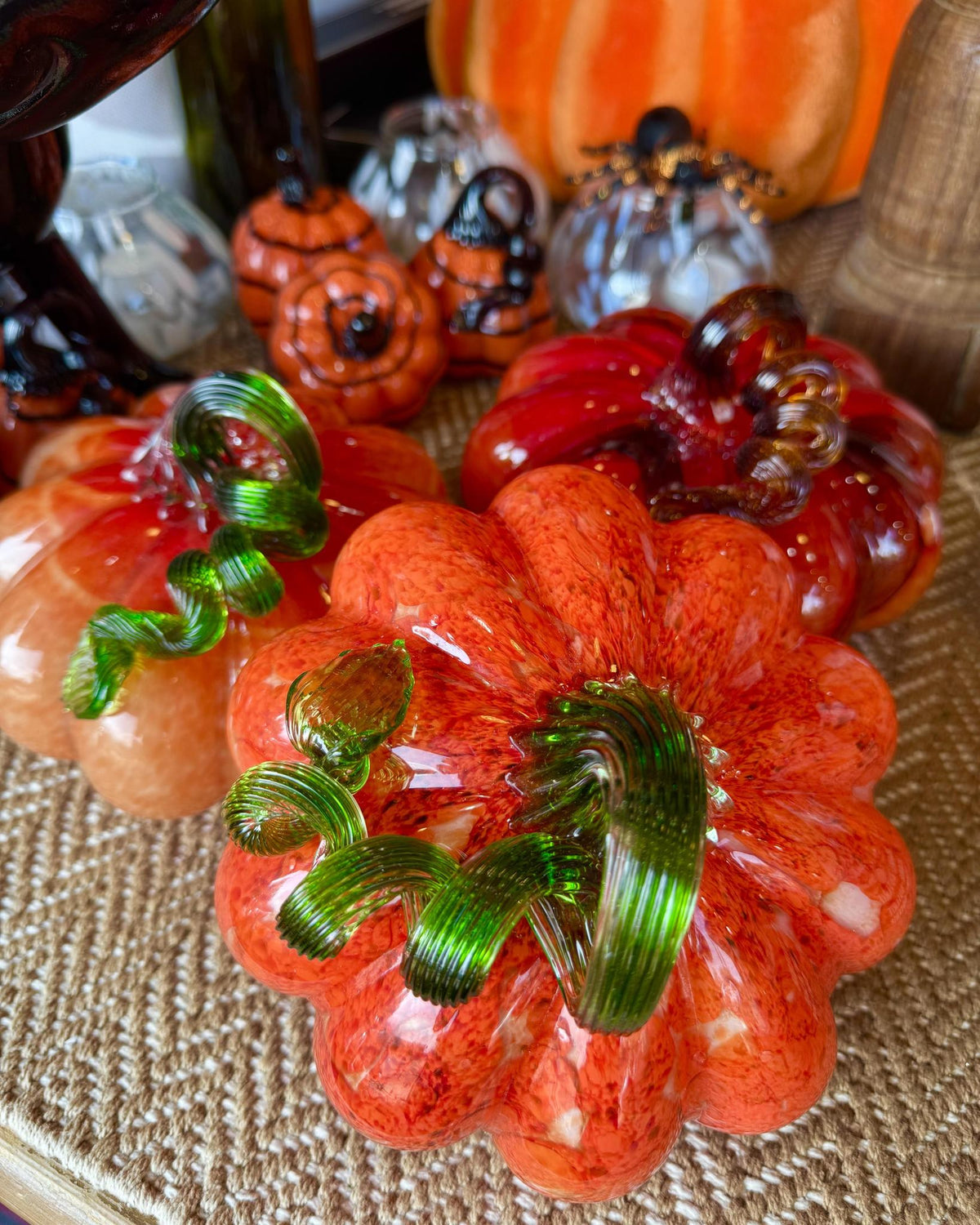 A set of hand-blown glass decorative pumpkins in autumn colors, including orange, red, and peach, with green glass stems.