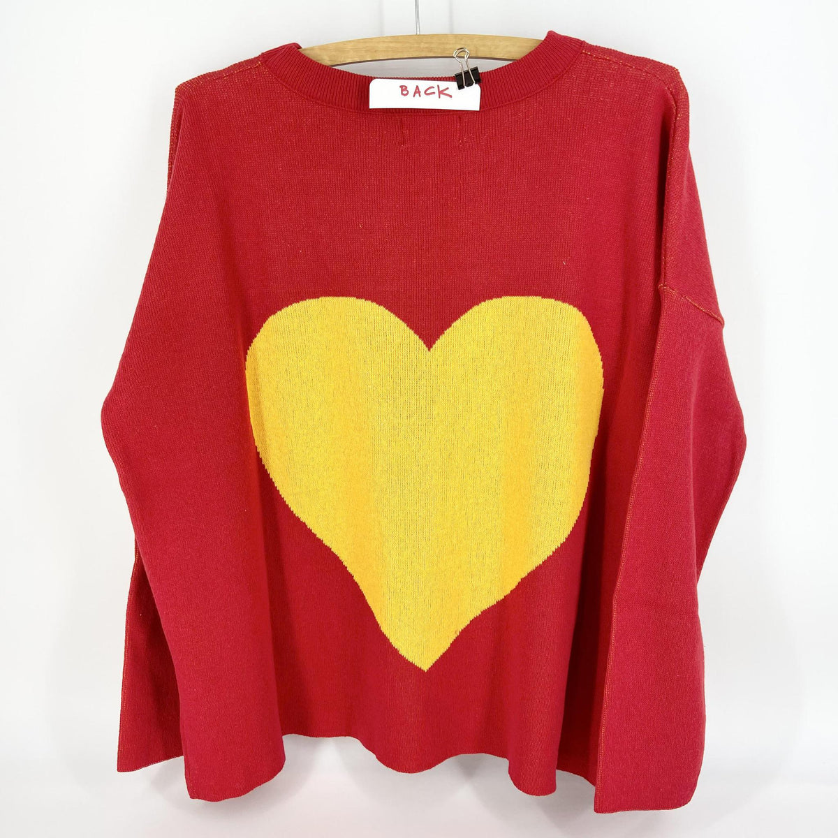 A red and gold pullover sweater with 'KC' text on the front and a heart shape on the back, displayed on a wooden hanger.